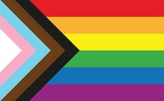A Progress Pride flag, featuring a triangle pointing to the right featuring transgender/intersex pride colors- pink, white, light blue- as well as Black and brown stripes to represent the BIPOC members of the LGBTQIA+ community, in addition to the traditional seven rainbow stripes.